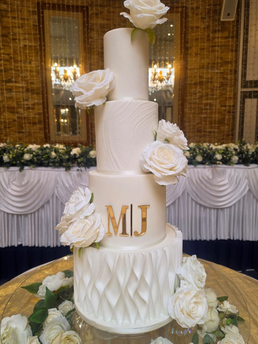 Four tier white wedding cake with white sugar roses and a gold monogram