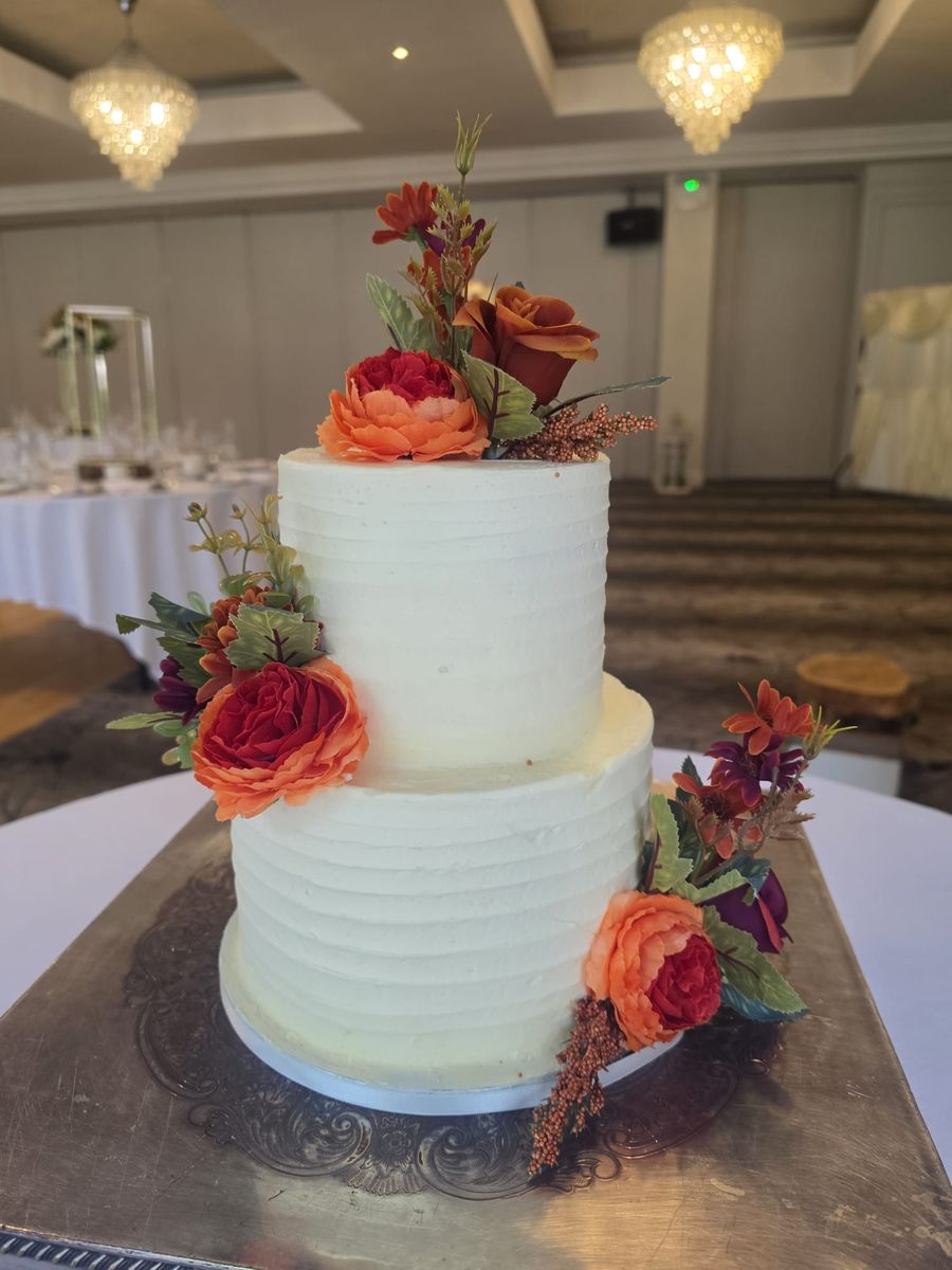 Two tier buttercream wedding cake with autumn flowers set up at a wedding venue
