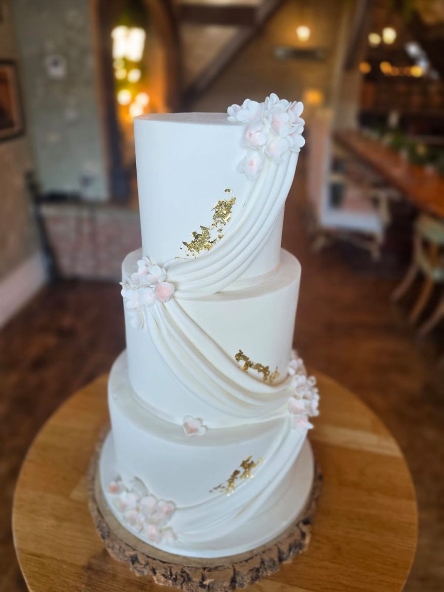 Three tier white wedding cake with draped sugar and gold leaf