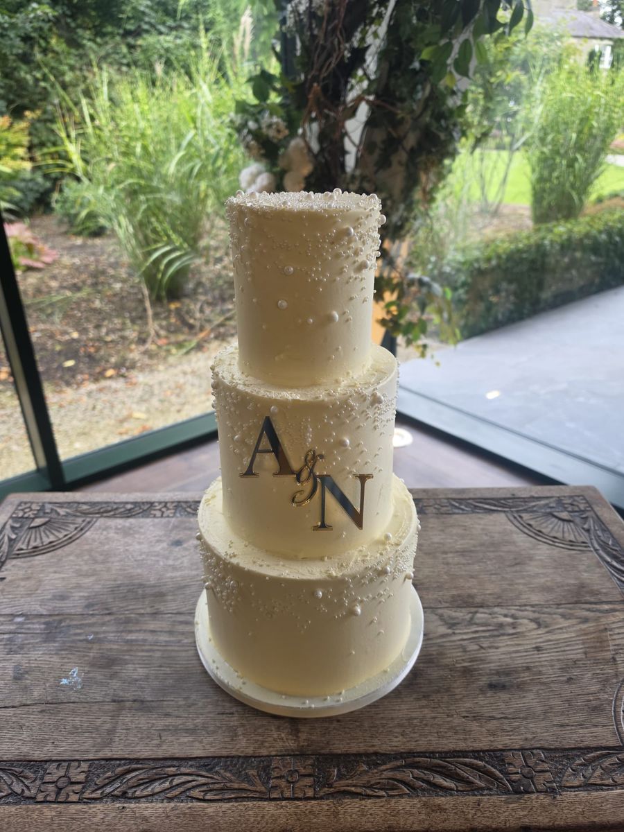 Three tier buttercream wedding cake scattered with pearls and a gold monogram