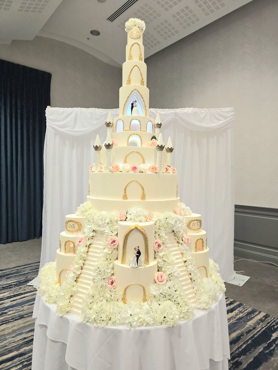 Ivory and gold castle wedding cake with turrets, lit archways, pink roses and grand staircases
