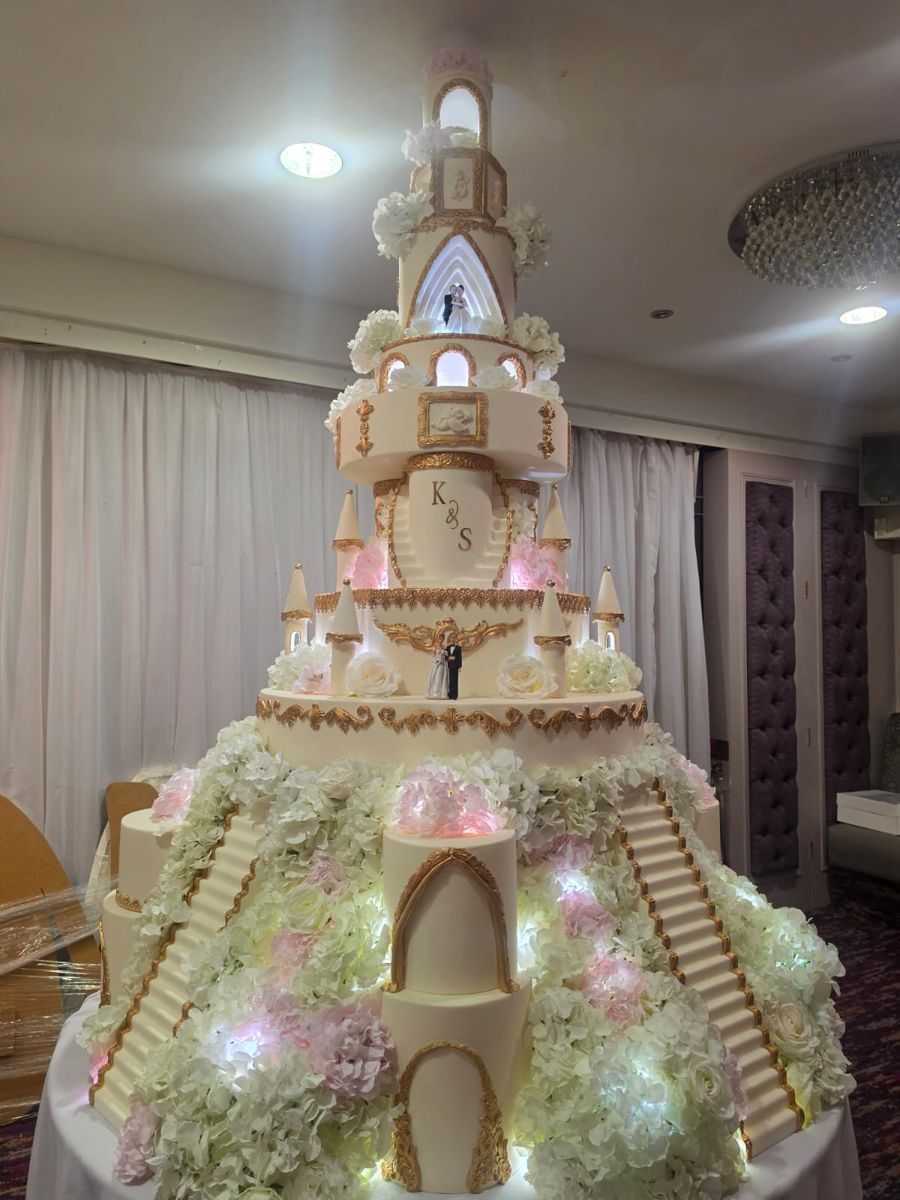 Cream and gold castle wedding cake with staircases, lit windows and pink and white hydrangeas