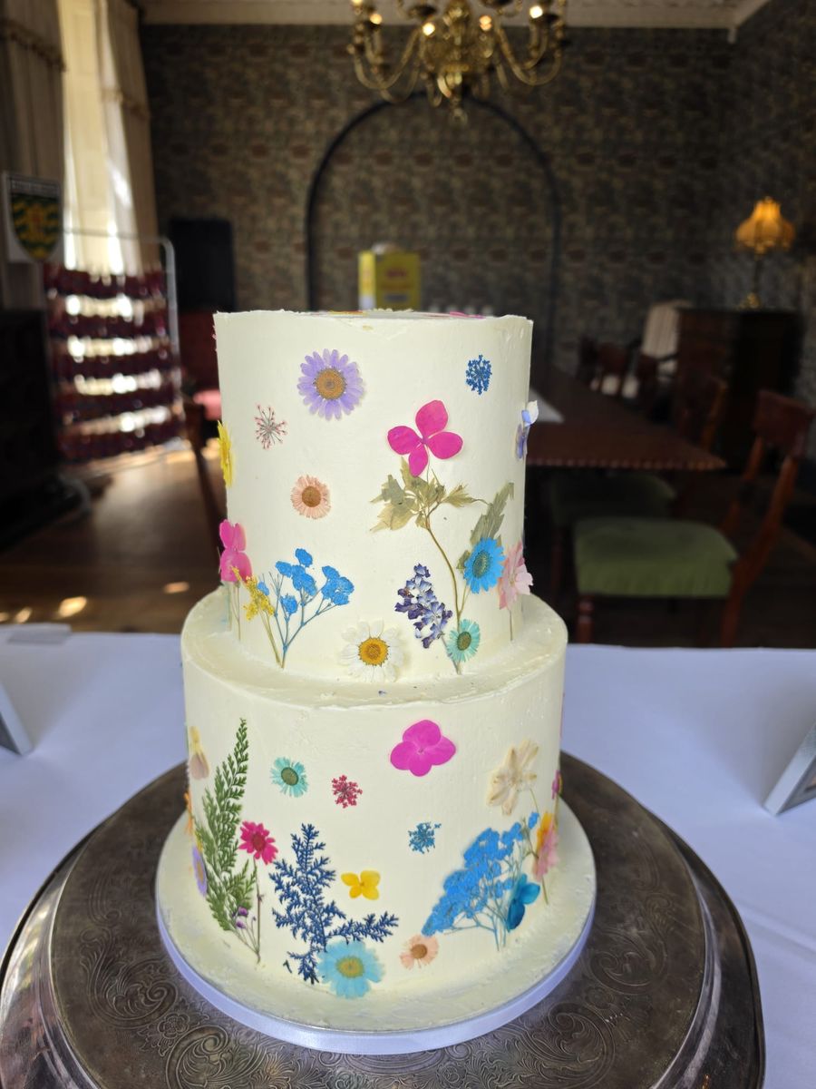 Two tier buttercream wedding cake decorated with colourful pressed wildflowers