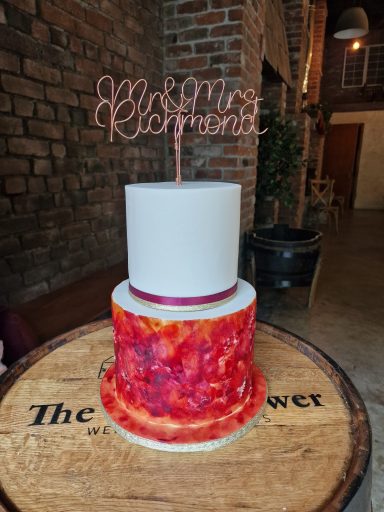 A two-tiered cake with a red marbled design and a pink topper that reads "Congratulations."