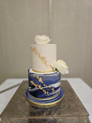 Three-tier wedding cake with blue marble design, gold accents, and white roses.
