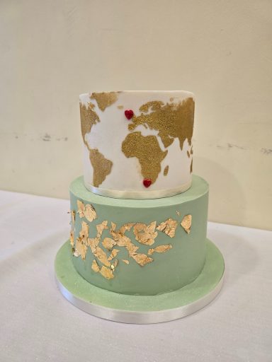 Two-tiered cake with a gold map design and red dots on the upper layer, mint green base.