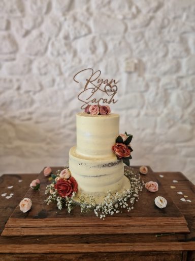 Two-tiered wedding cake adorned with flowers and a "Happy Birthday" topper.