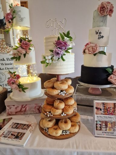 A display featuring multiple wedding cakes and a tiered donut stand decorated with flowers.