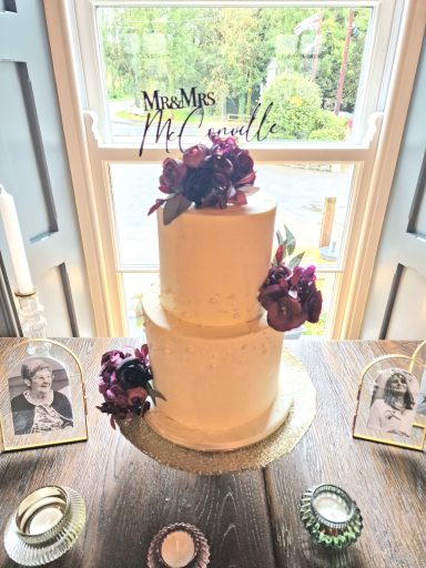 Two-tier wedding cake decorated with flowers, displayed on a wooden table.